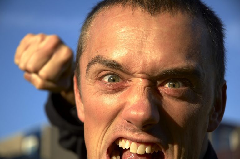 a close up of an angry man's face with mouth open shouting and raising his fist