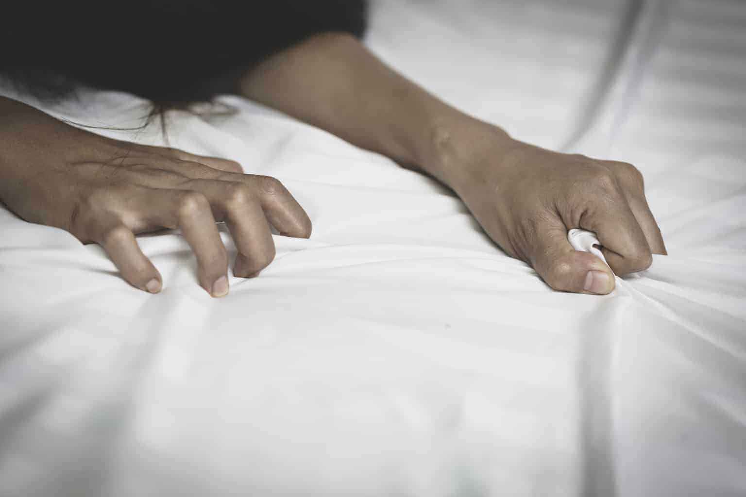A woman's hands grabbing sheets on a bed