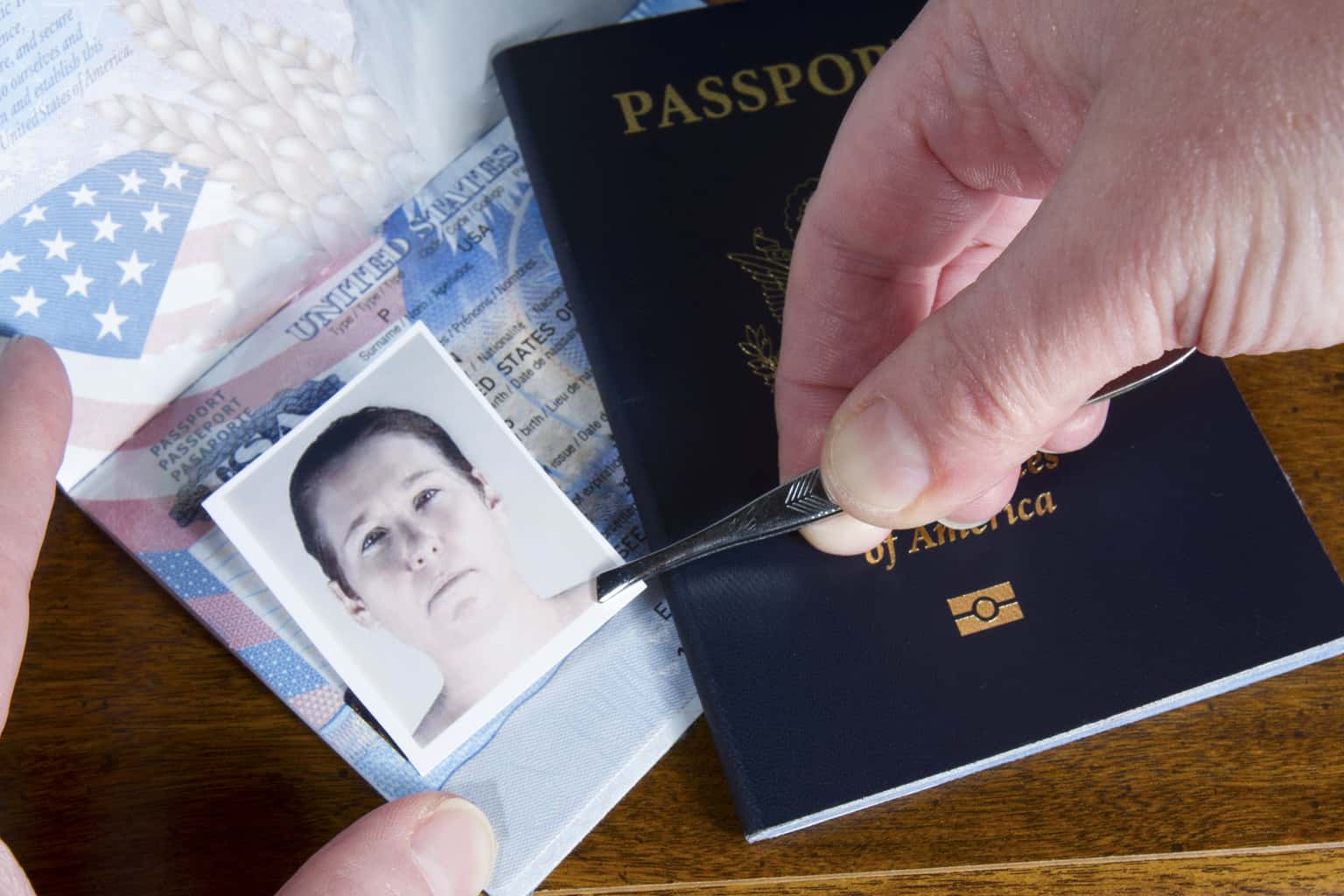 A man's hands using tweezers to place an image over a photo on a passport.