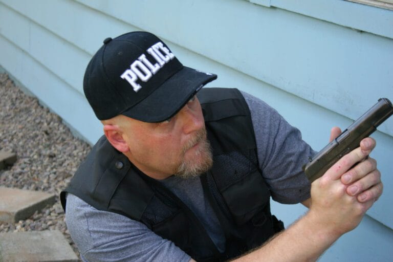 An officer squats with gun drawn. New technology could allow him to write a police report based on statements he makes into his bodycam.