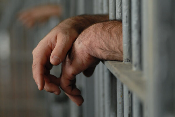 A man's hands hanging outside prison cell bars